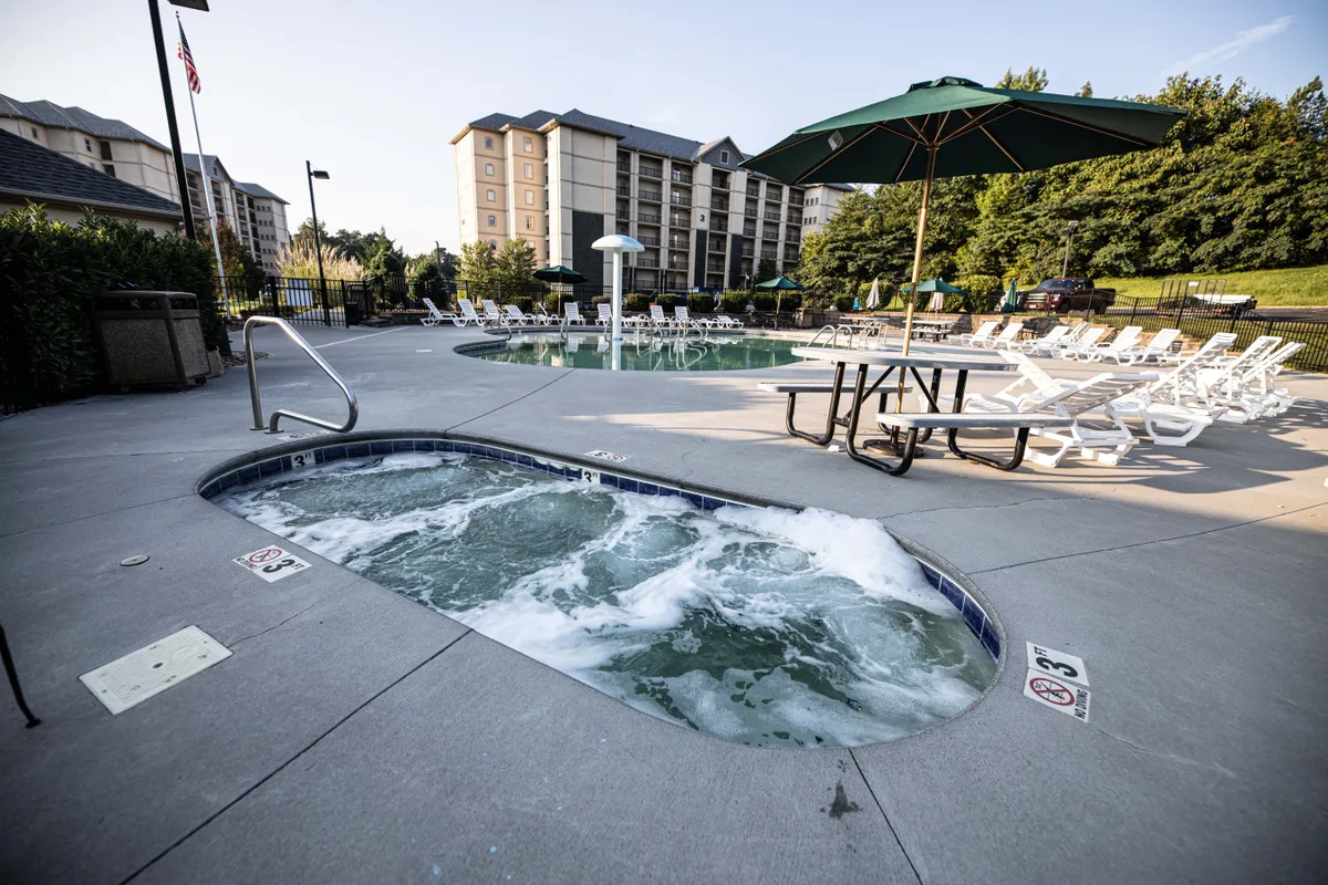 This exterior shot features a lively resort pool scene with a large hot tub, a swimming pool surrounded by lounge chairs and umbrellas, and a picnic table for outdoor gatherings. The setting is inviting and tranquil, ideal for sunbathing, swimming, or unwinding in the hot tub.