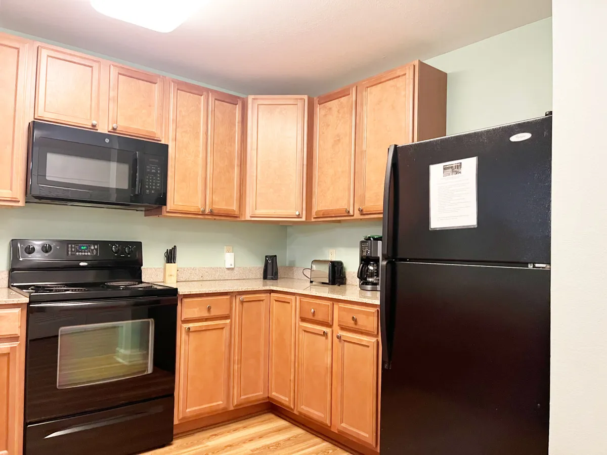 The image showcases a warm, inviting kitchen with sleek black appliances, rich wooden cabinetry, and elegant granite countertops, creating a perfect space for cooking, gathering, and sharing meals. The cozy atmosphere hints at memorable moments spent with family and friends.
