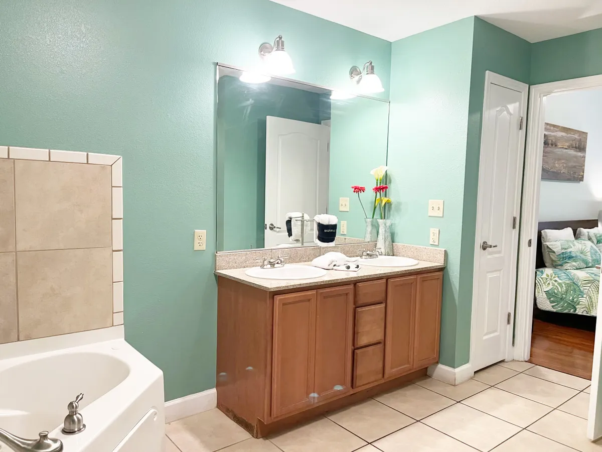 A spacious bathroom featuring a double sink vanity, a large mirror, a bathtub, and a floral arrangement. The clean lines and soothing colors evoke a spa-like atmosphere, perfect for both relaxation and efficient morning routines.