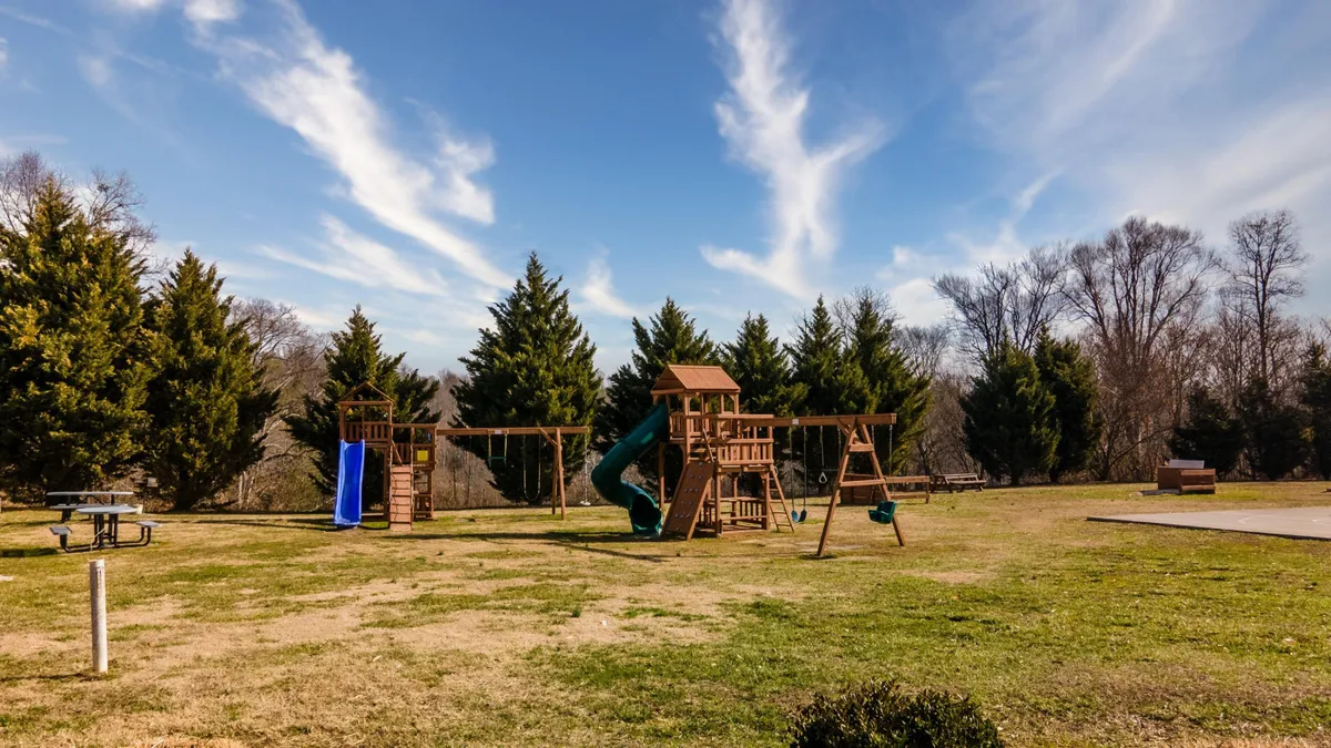 A cheerful scene of a playground with swings and a slide, inviting children and families to engage in outdoor play. The surrounding open area is suitable for picnics and casual family gatherings, amplifying the family-friendly vibe.