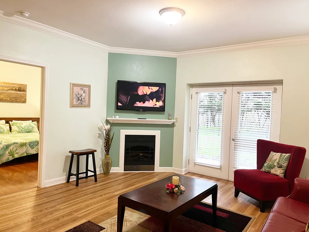 A cozy living room setup with a TV displaying a romantic scene, a plush red armchair, and a coffee table adorned with decorative items. The ambiance is intimate and inviting, perfect for relaxing evenings or downtime between adventures.