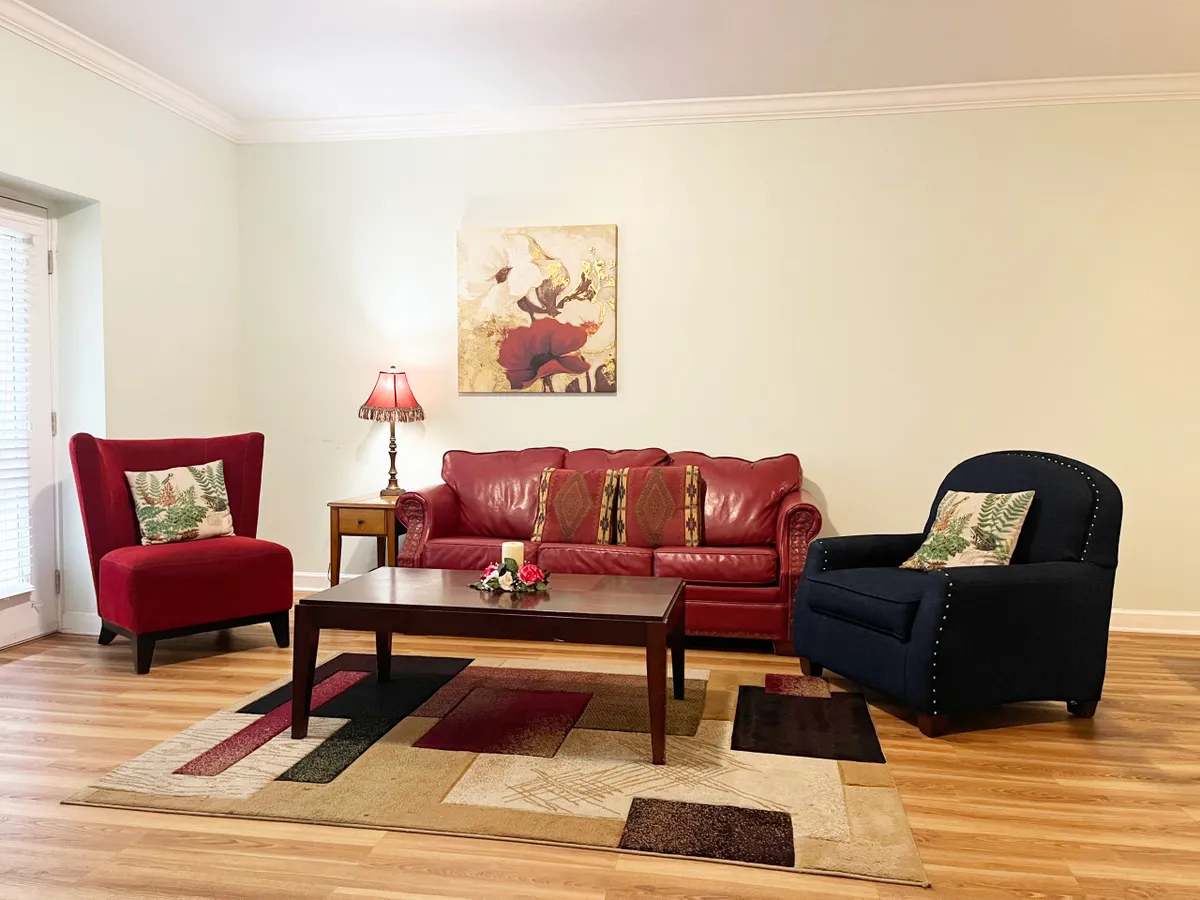 This image captures a cozy living room featuring a red sofa, blue chair, coffee table with a floral arrangement, and tasteful artwork on the wall. The layout invites both relaxation and conversation, embodying the concept of a private yet inviting retreat.
