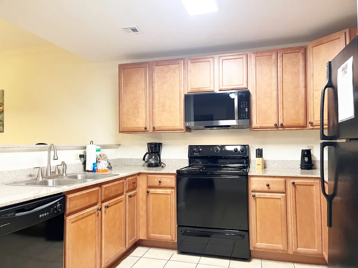 This image centers on a modern kitchen with kitchen cabinets, stainless steel appliances, and a granite countertop with a sink. The kitchen appears well-equipped and spacious, ideal for cooking and gathering. The warm lighting and uncluttered surfaces evoke a welcoming mood, showcasing the space's readiness for group meal prep or morning coffee routines.